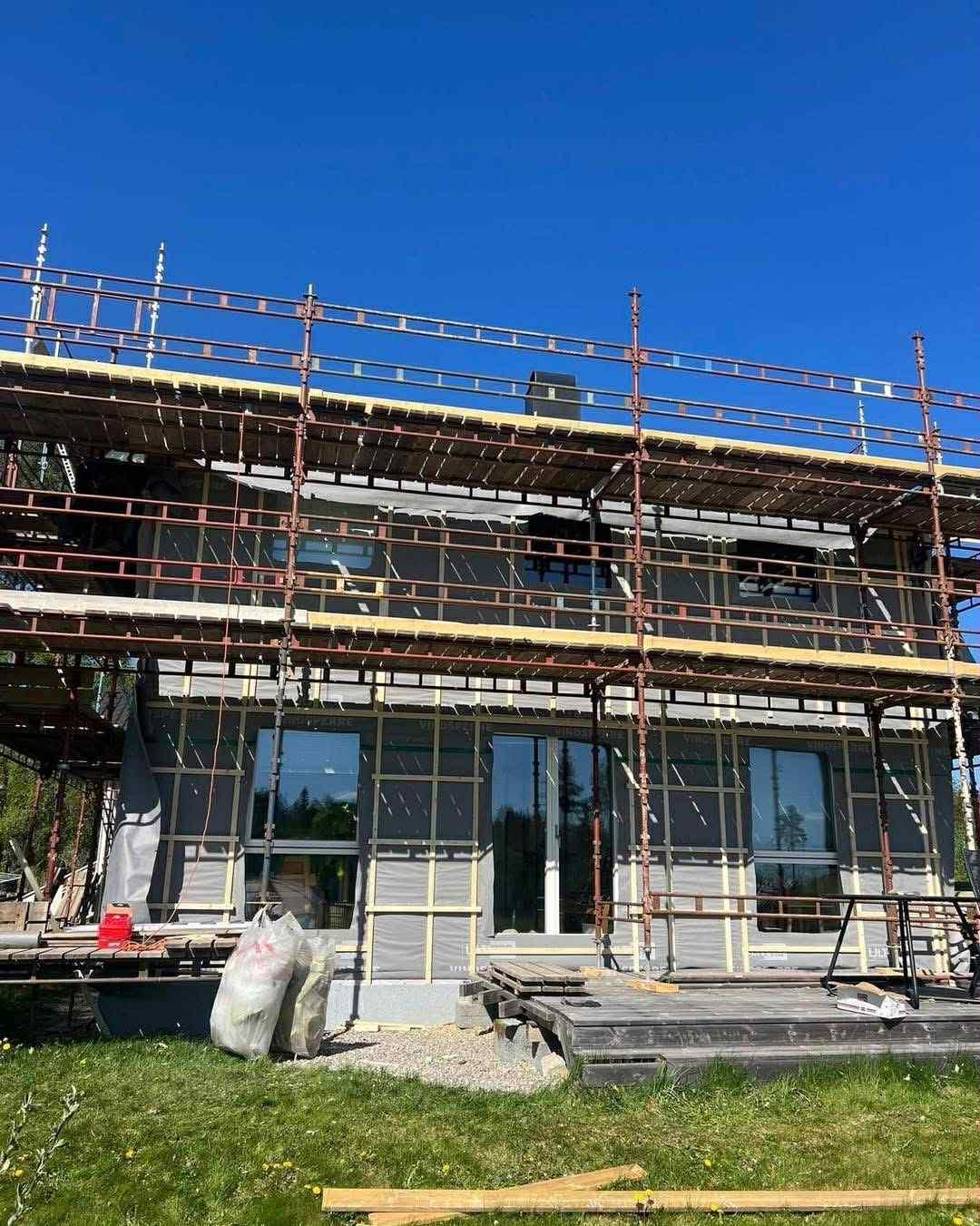 Et hus under arbeid, med stillas rundt og vindsperre på veggene
